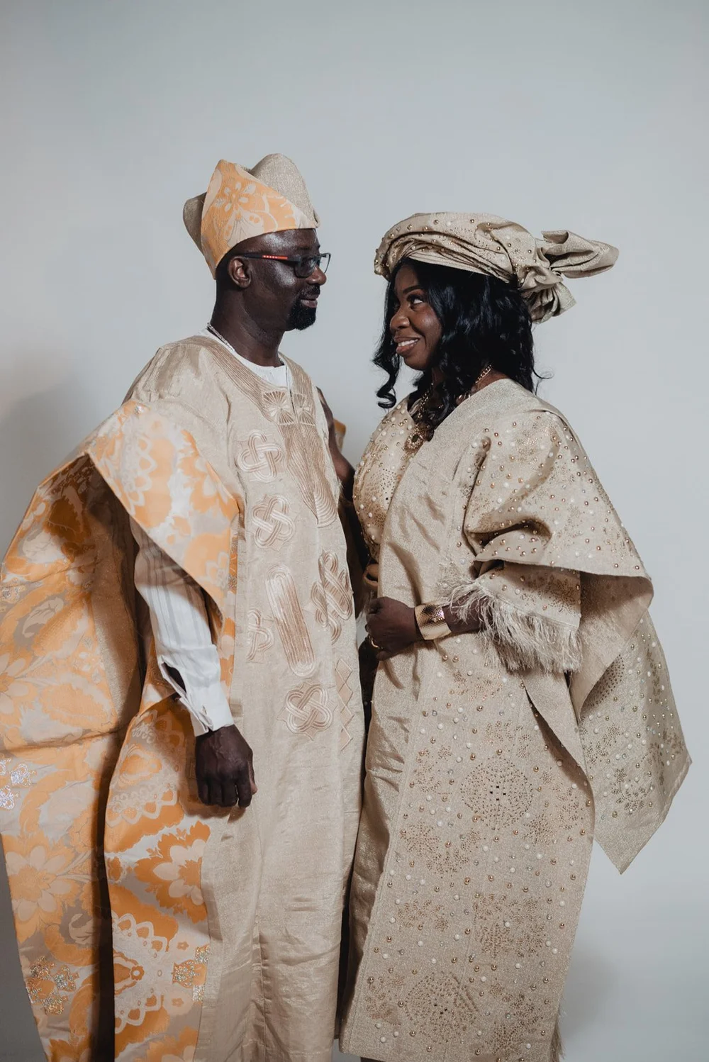 Bride and groom in matching aso-oke facing one another, the groom’s embroidered agbada falling from his shoulder
