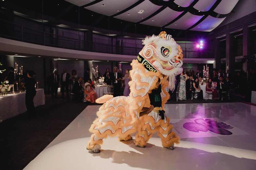 Orange lion performing under the reception lights on the white dance floor