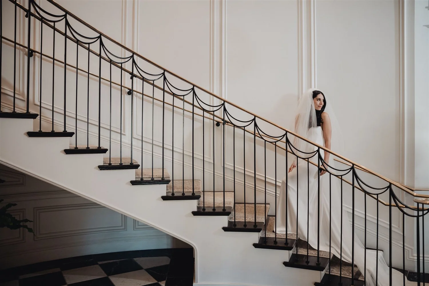 Bride on the curved Manor House staircase at Rosewood Miramar Beach, the black scalloped ironwork running beside her