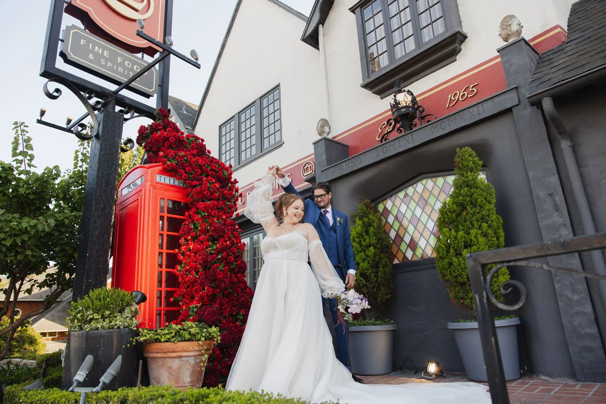 The Tudor-style front of Five Crowns in Corona del Mar, with a red phone box wrapped in roses and the couple beside it