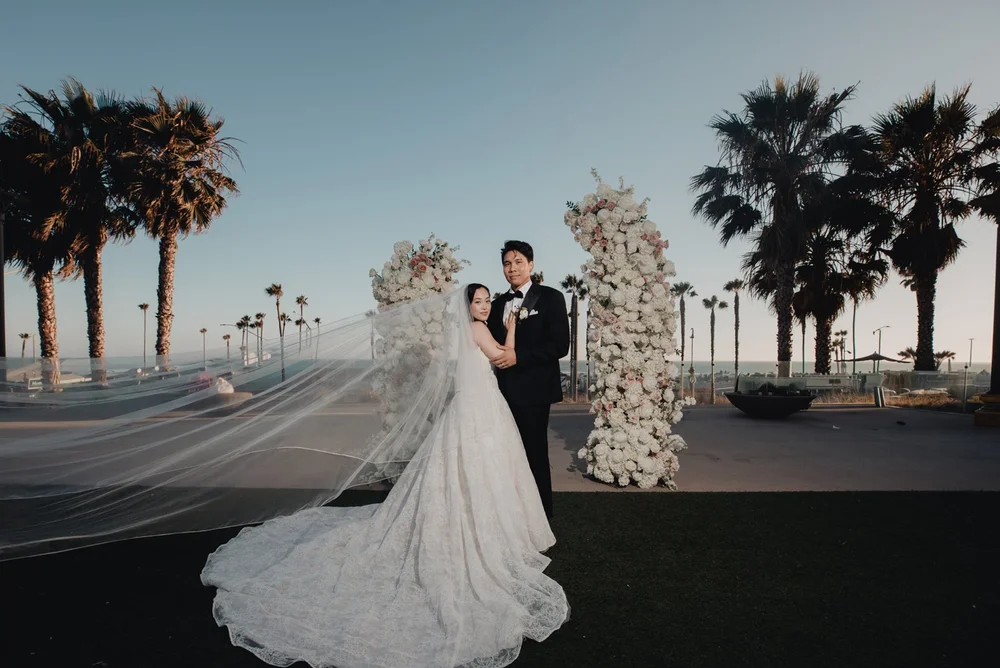 Couple beside a floral pillar on the ocean-view deck at Pasea Hotel, veil in the wind