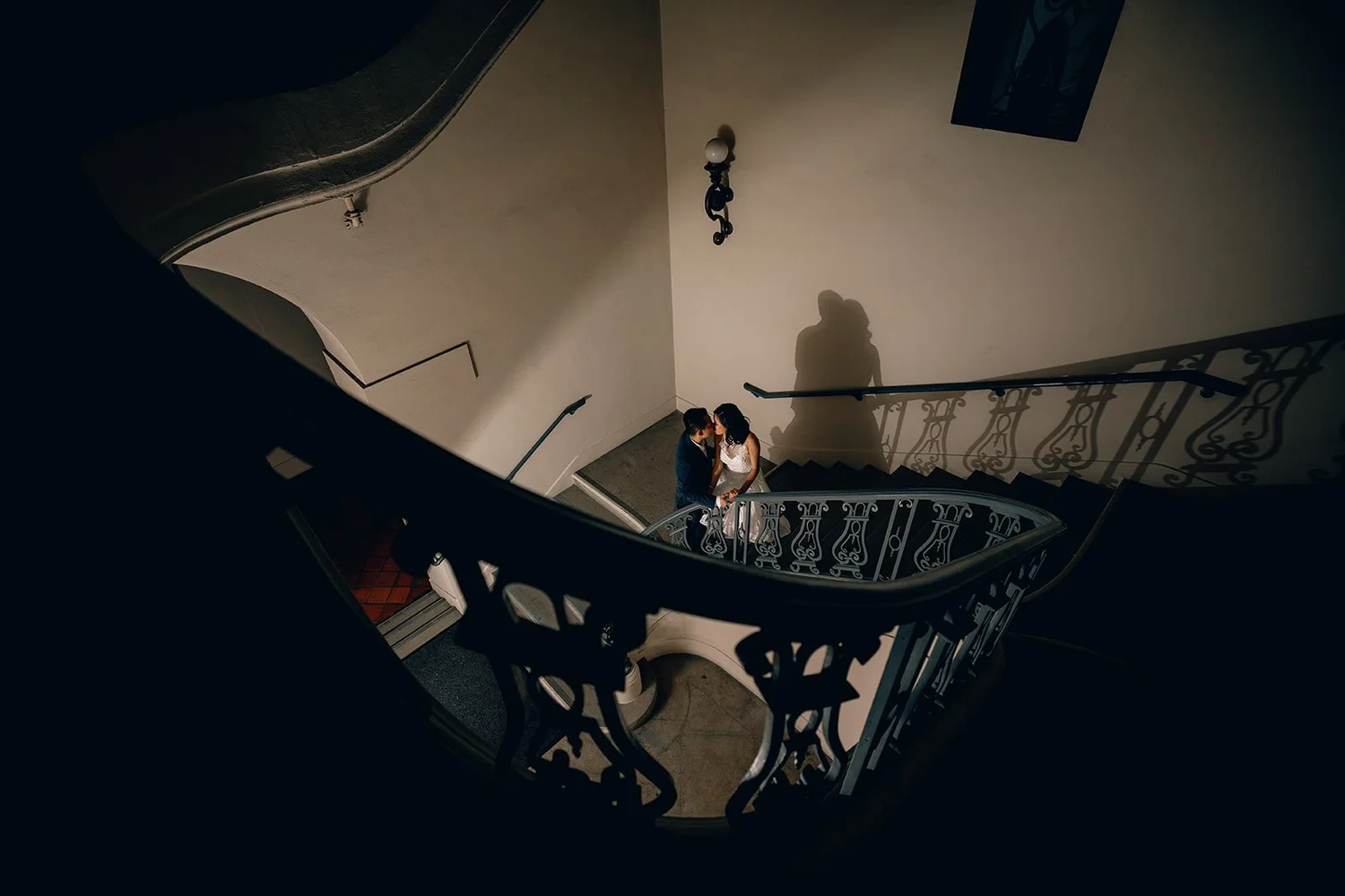 Couple embracing on the landing of the curved wrought-iron staircase inside Pasadena City Hall