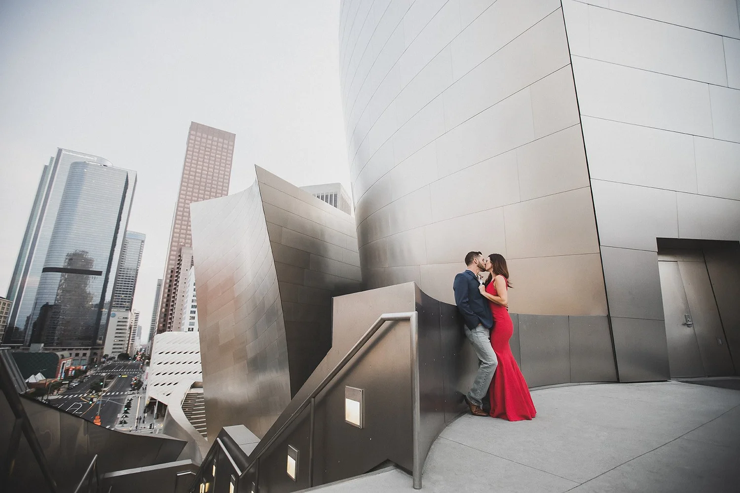 Couple against the stainless steel of Walt Disney Concert Hall with the downtown Los Angeles towers rising behind them