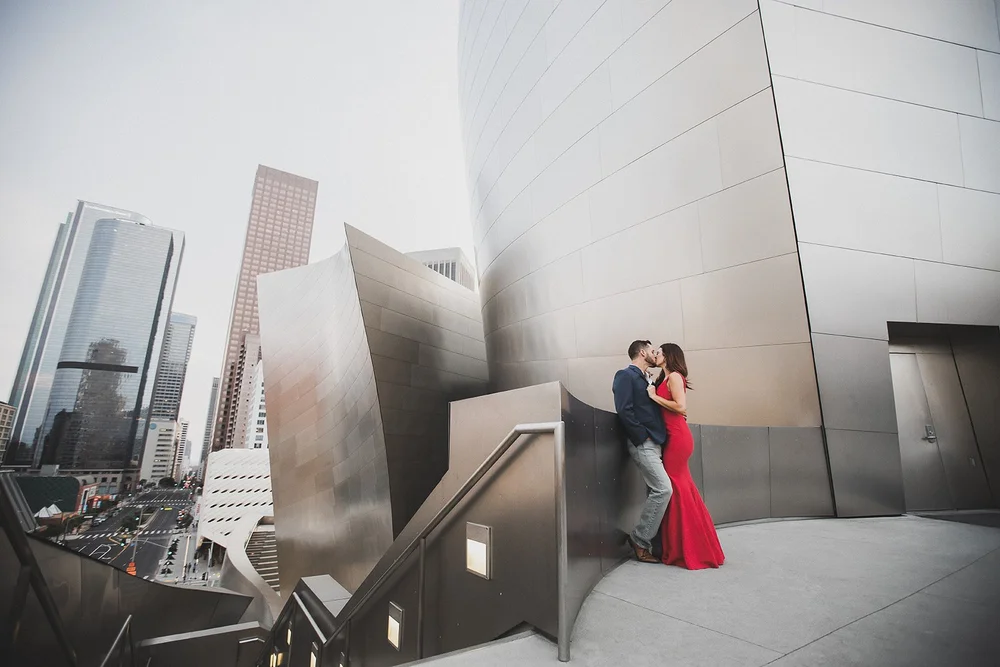 Couple against the stainless steel of Walt Disney Concert Hall with the downtown Los Angeles towers behind