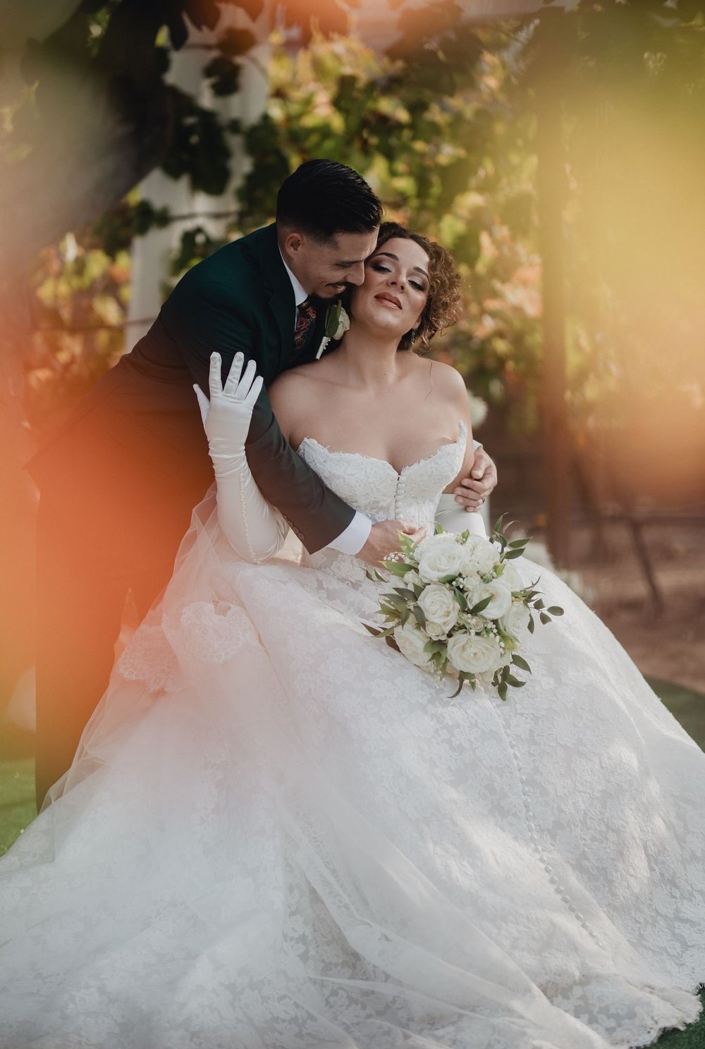 Bride in a corseted 3D floral ball gown seated with her husband under a warm garden canopy