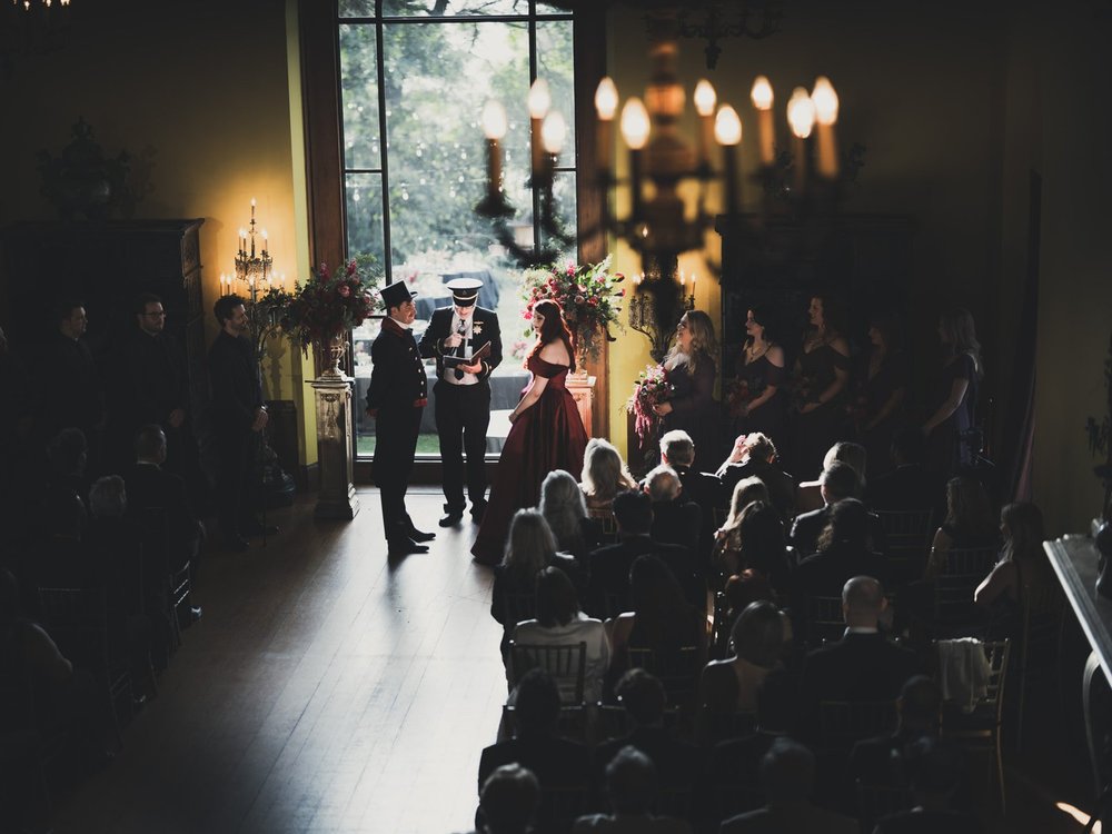 Candlelit indoor ceremony at the Paramour Estate, guests seated either side of a dark aisle