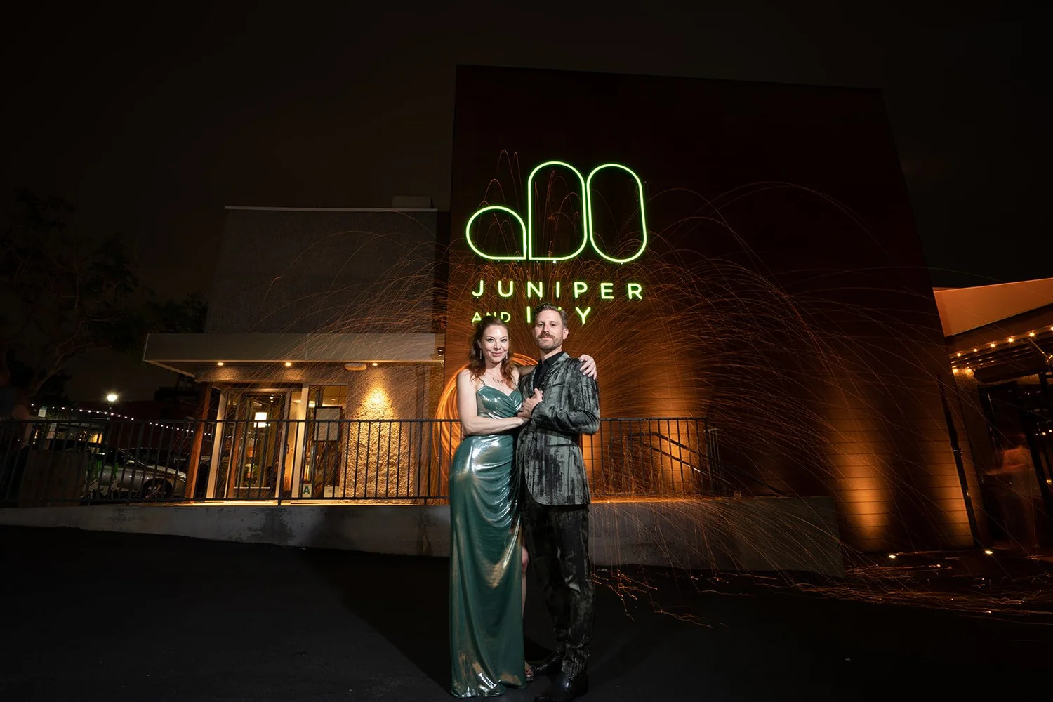 Couple in front of the green neon monogram outside Juniper and Ivy in Little Italy, San Diego, sparks trailing behind them