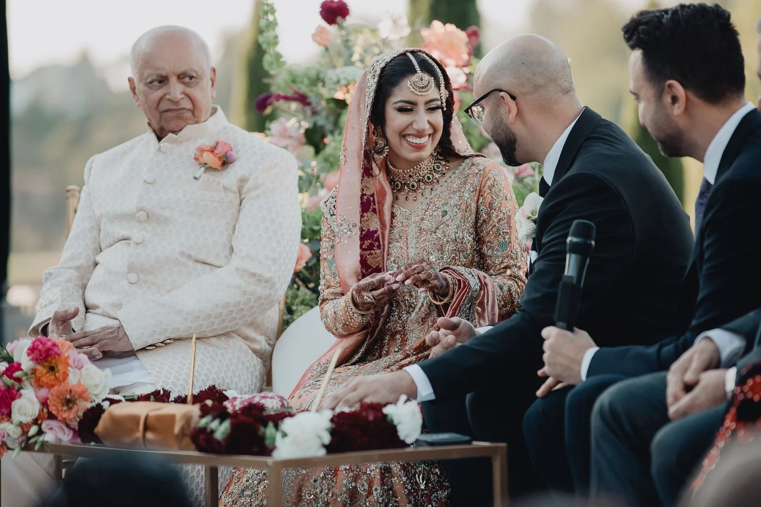 Bride smiling during the nikah beside her grandfather and the groom on an outdoor stage