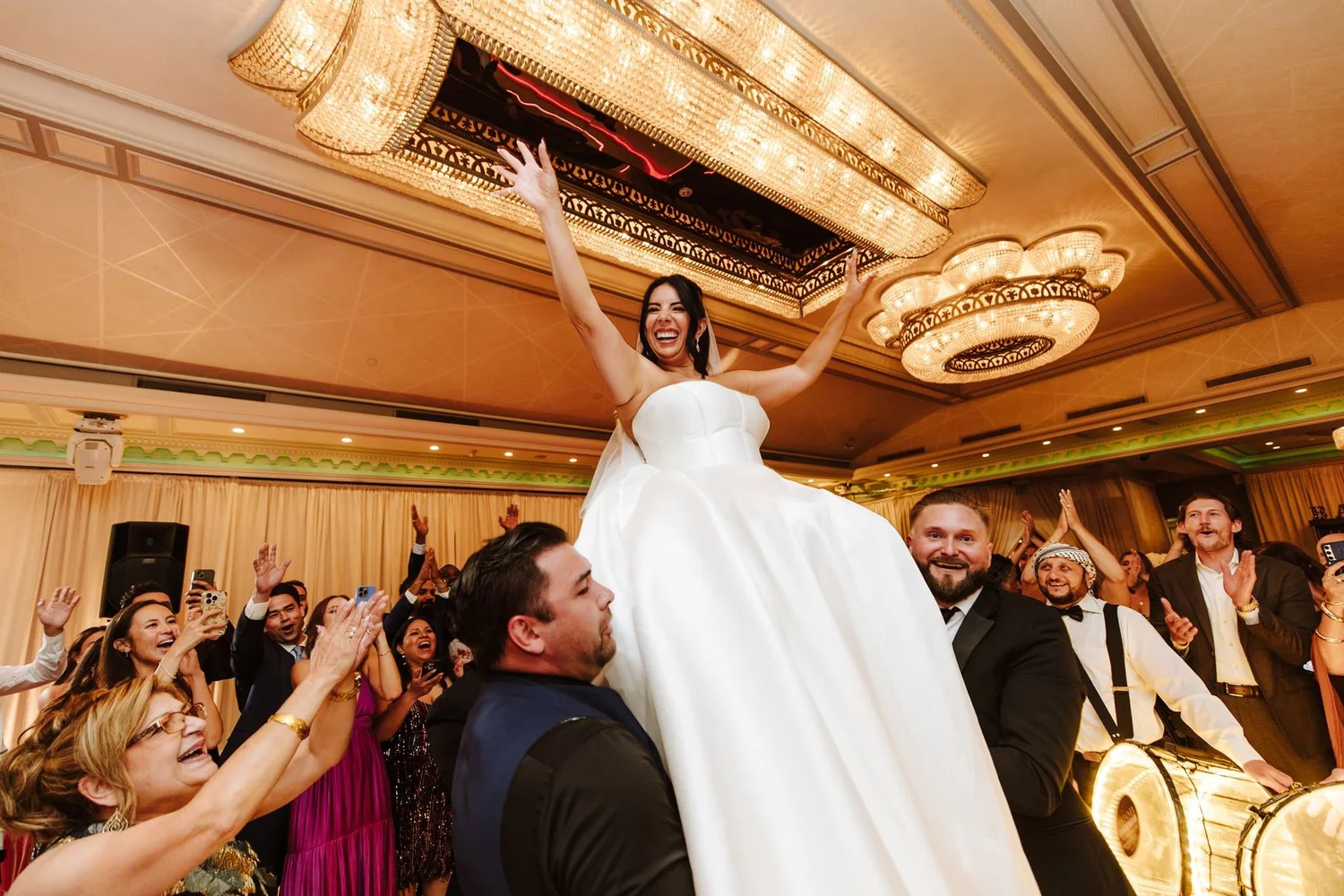 Bride lifted on shoulders by cheering guests under the ballroom lights at Glenoaks Ballroom