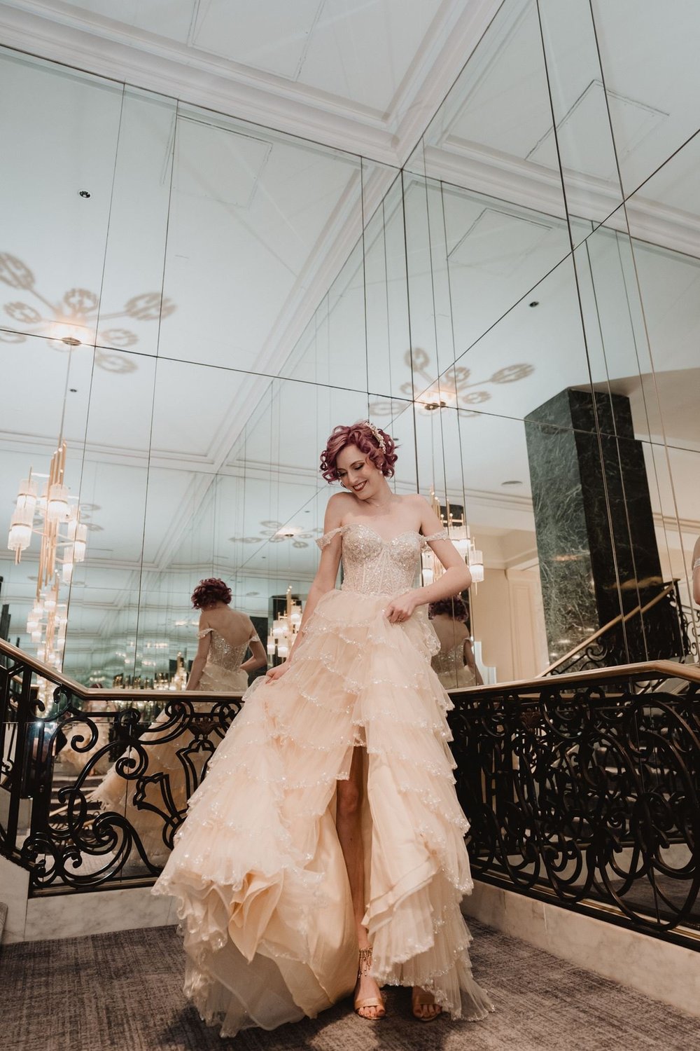 Bride in a blush ruffled gown with a thigh-high slit posed against a mirrored hotel wall