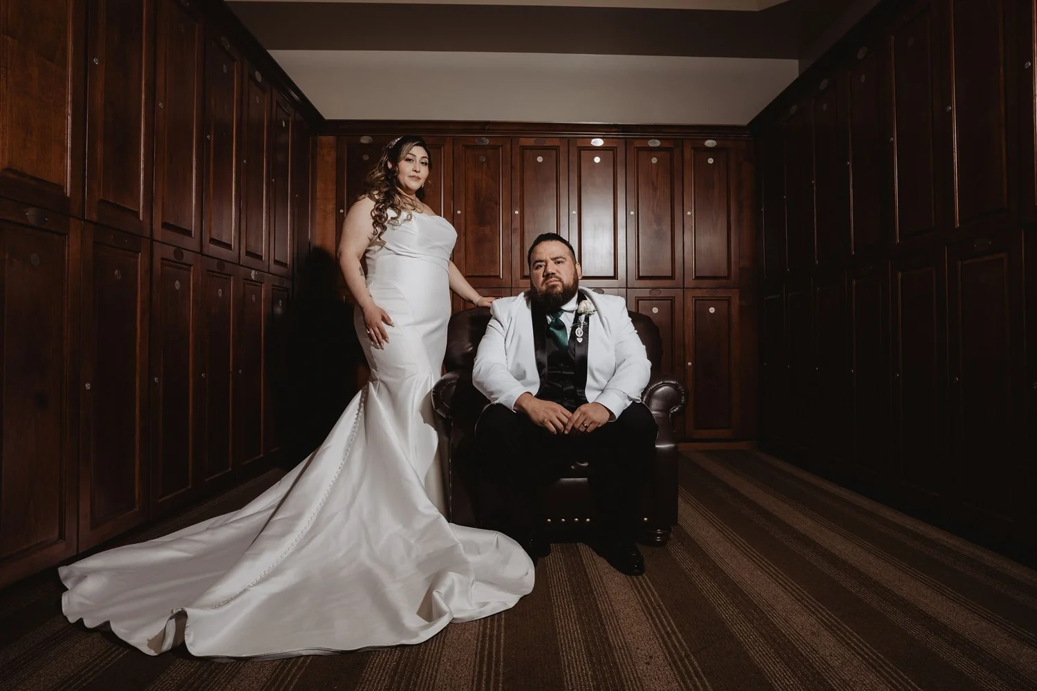 Bride standing by the groom seated in a dark paneled room at Vellano Estate