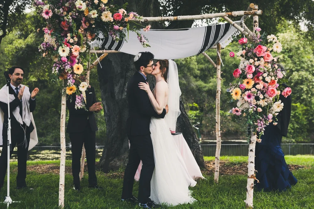 Couple kissing under a birch chuppah dressed with wildflowers