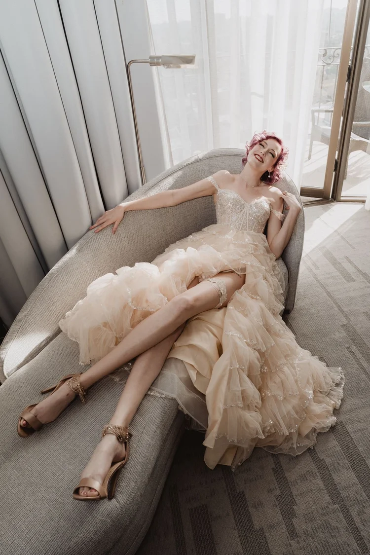 Bride in a blush ruffled gown reclining on a sofa with the ruffled skirt spread across the seat