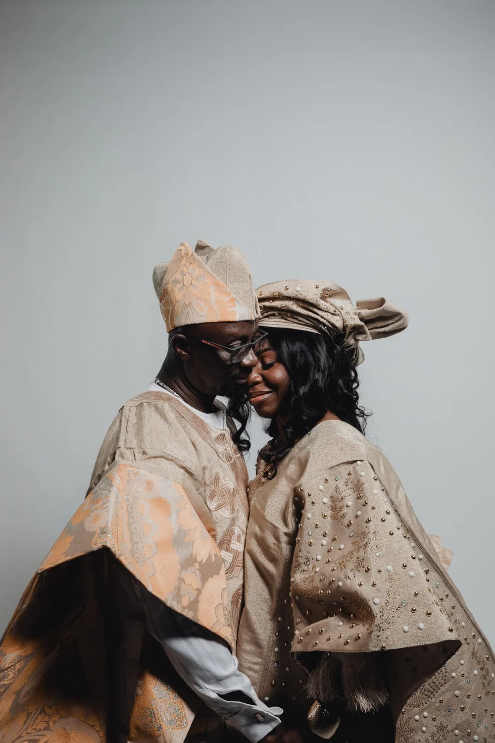 Nigerian couple forehead to forehead with eyes closed, the bride’s beaded sleeve catching the light