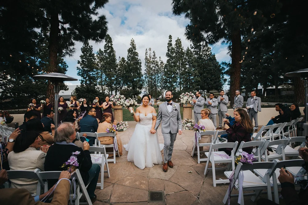Newlyweds walking the recessional aisle at Turnip Rose Promenade and Gardens as guests applaud