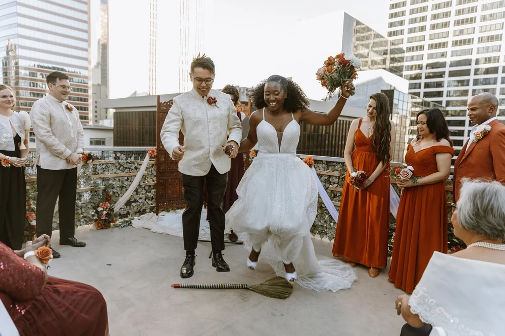 Couple jumping the broom as their bridal party cheers at a Nigerian and Filipino wedding