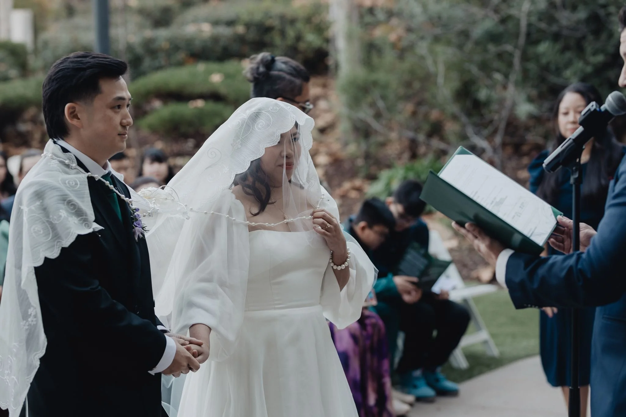 Secondary sponsors draping the wedding veil over the bride and groom during a Filipino Catholic ceremony