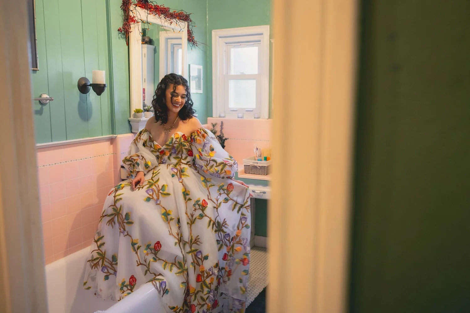 Bride in a floral gown seated in a pink and green room, framed through a doorway at The Hacienda