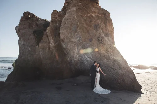 Bride photographed small against a sea rock on the Malibu coast