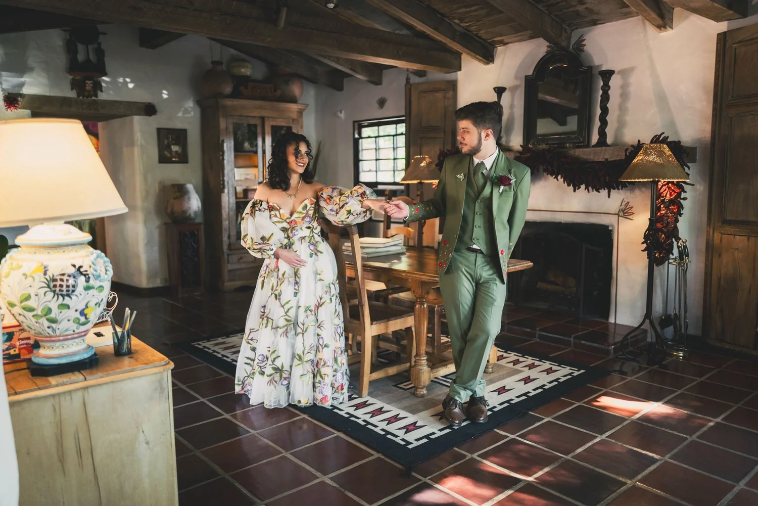 Couple holding hands in the tiled living room with a fireplace and beamed ceiling at The Hacienda