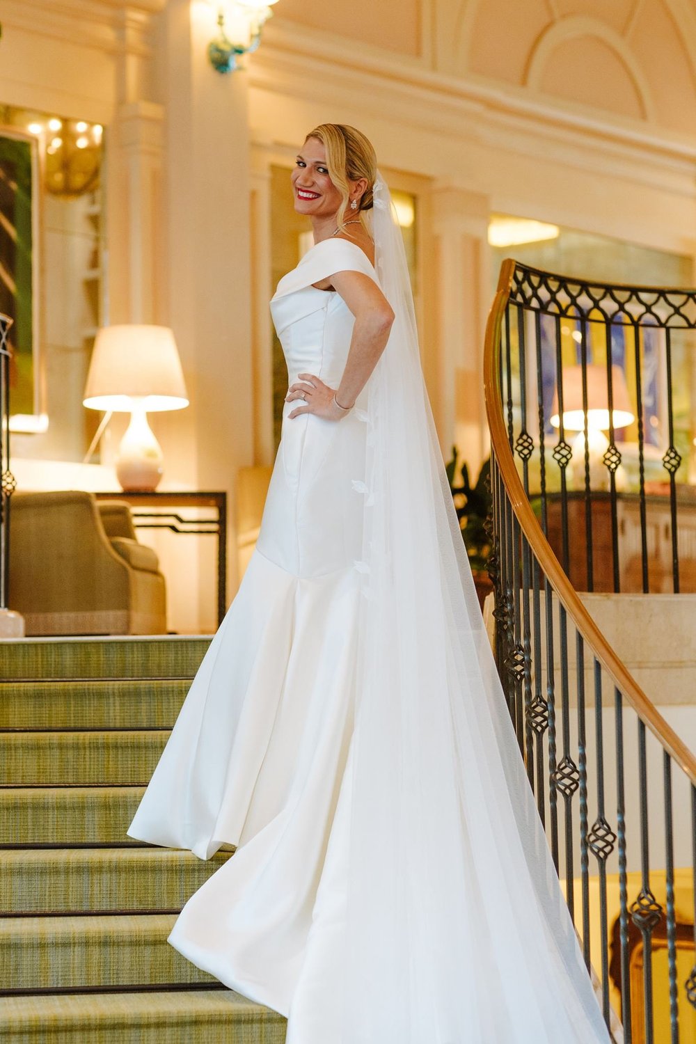 Bride in a white silk fit-and-flare gown cascading a cathedral train down a grand hotel staircase