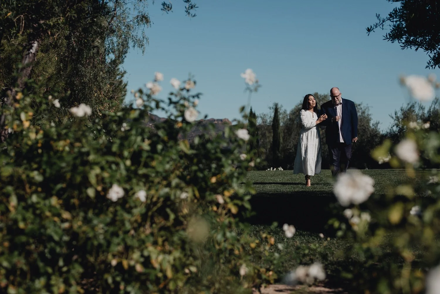 Couple on a garden lawn behind white roses at a private estate in the Malibu hills