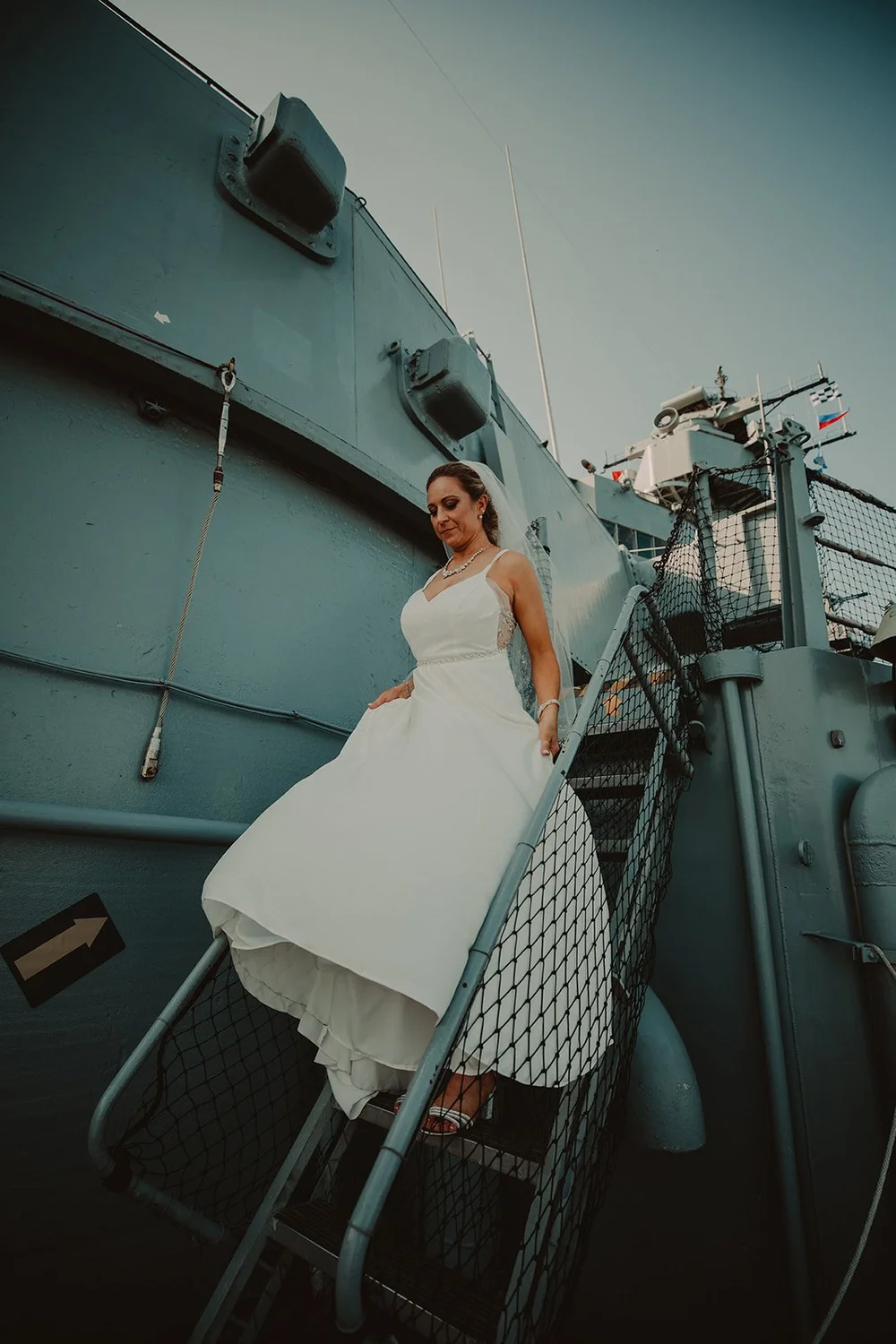 Bride on a painted steel stairway inside the Queen Mary with her train falling down the steps