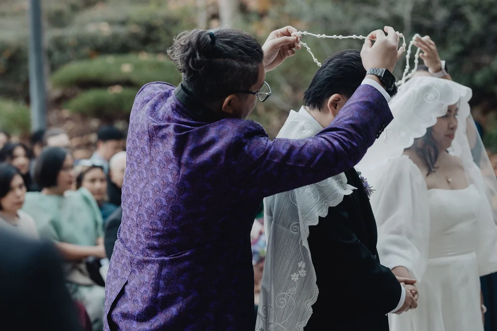 Sponsor lowering the nuptial cord over the shoulders of the bride and groom