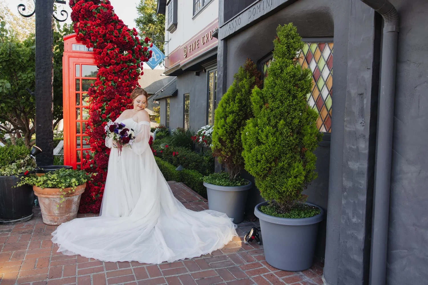 Bride seated on the brick walk by the red phone box and potted topiaries at Five Crowns