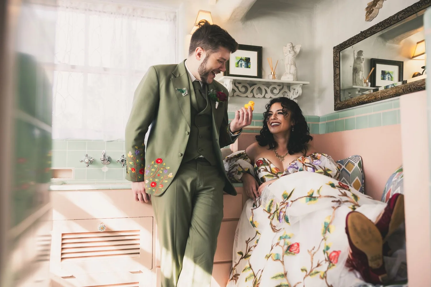 Groom laughing with the bride in her floral gown in a pastel room with a window seat at The Hacienda