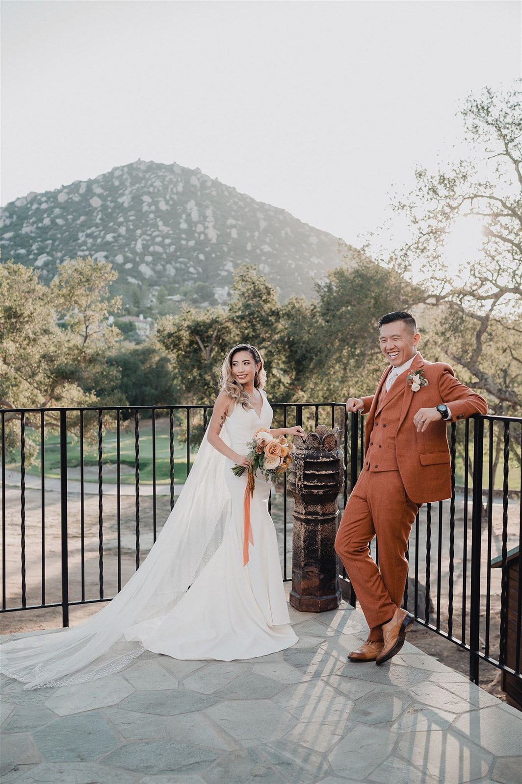 Bride and groom at the stone terrace railing at Mt. Woodson Castle, the granite dome of Mt. Woodson rising behind them