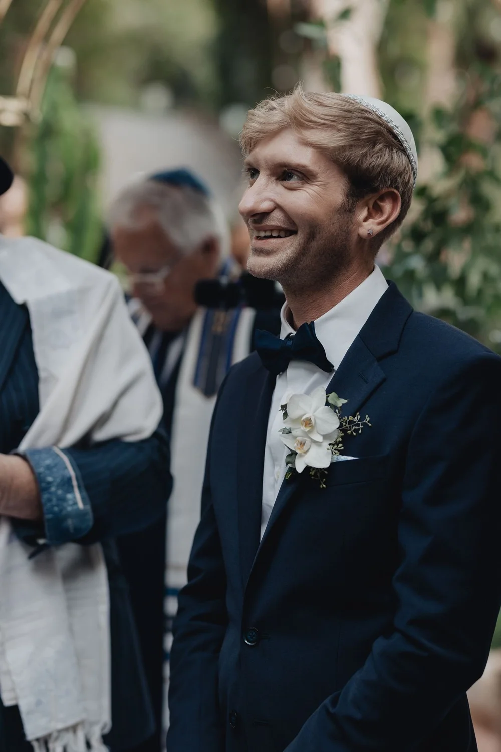Groom in a kippah smiling as he waits beneath the chuppah