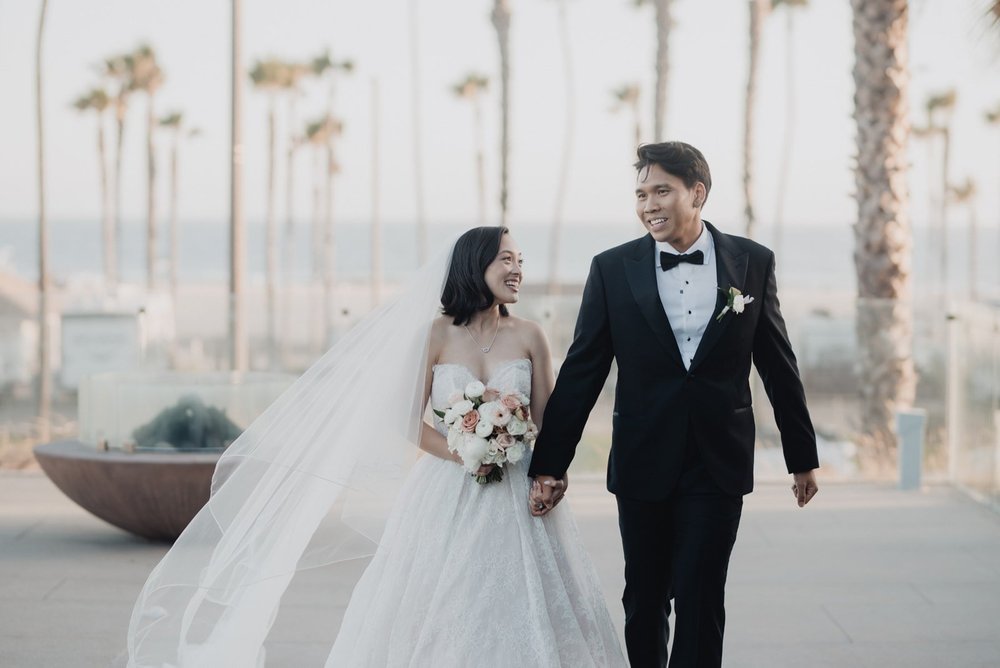 Bride and groom walking hand in hand with Huntington Beach behind them