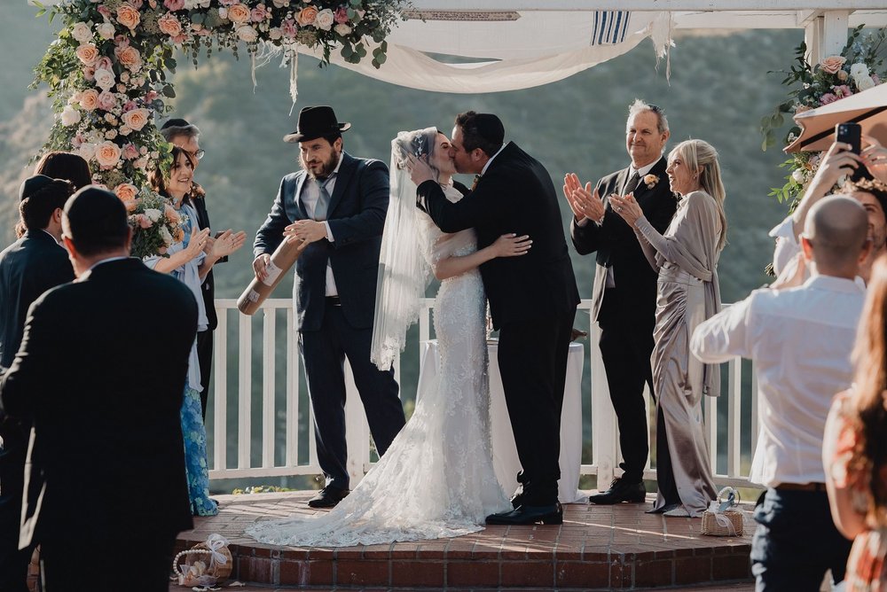 Couple kissing on the ceremony platform as guests applaud after the breaking of the glass