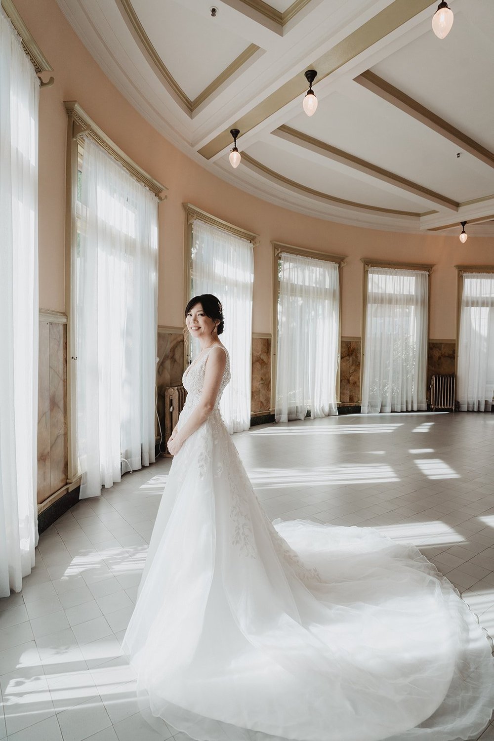 Back view of an A-line wedding dress with a wide tulle chapel train fanned across a sunlit ballroom floor