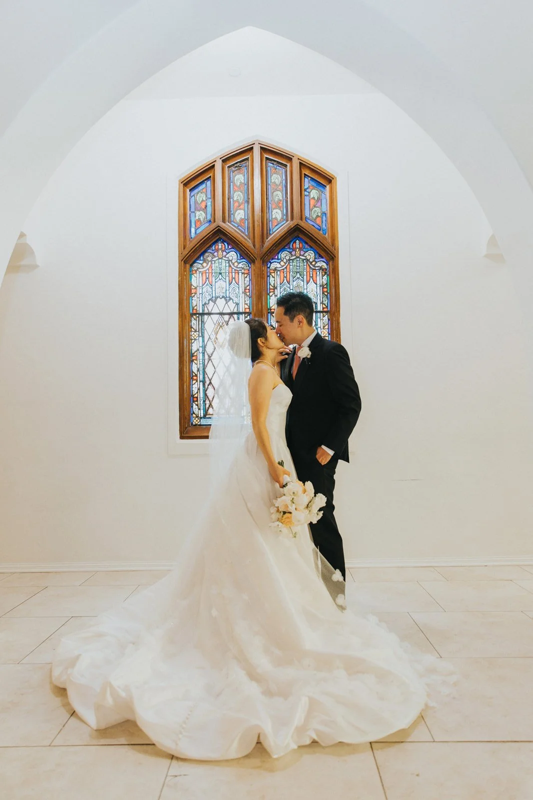 Couple beneath the stained glass window in the white chapel at The Sanctuary, Long Beach
