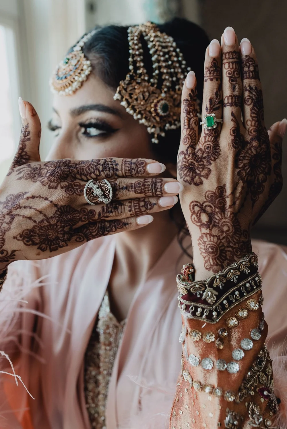Bride framing her face with henna-covered hands, a jeweled matha patti on her brow