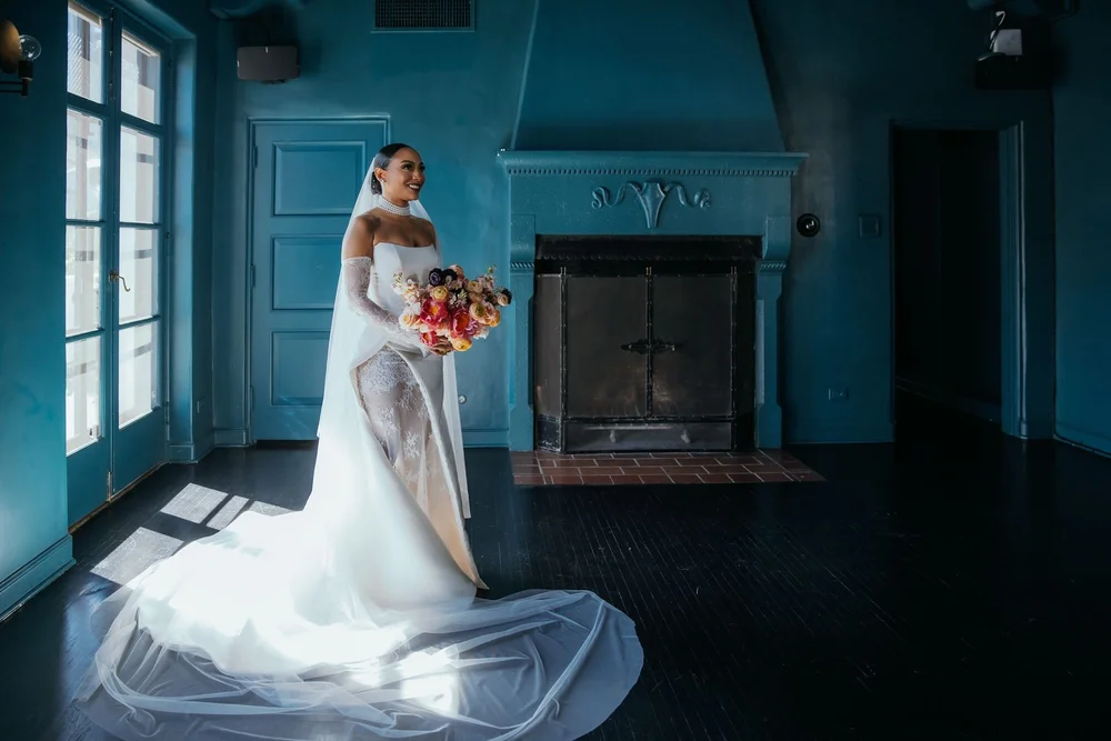 Full-length frame of a bride in a fitted gown with a detachable chapel train and veil pooled across a wooden floor