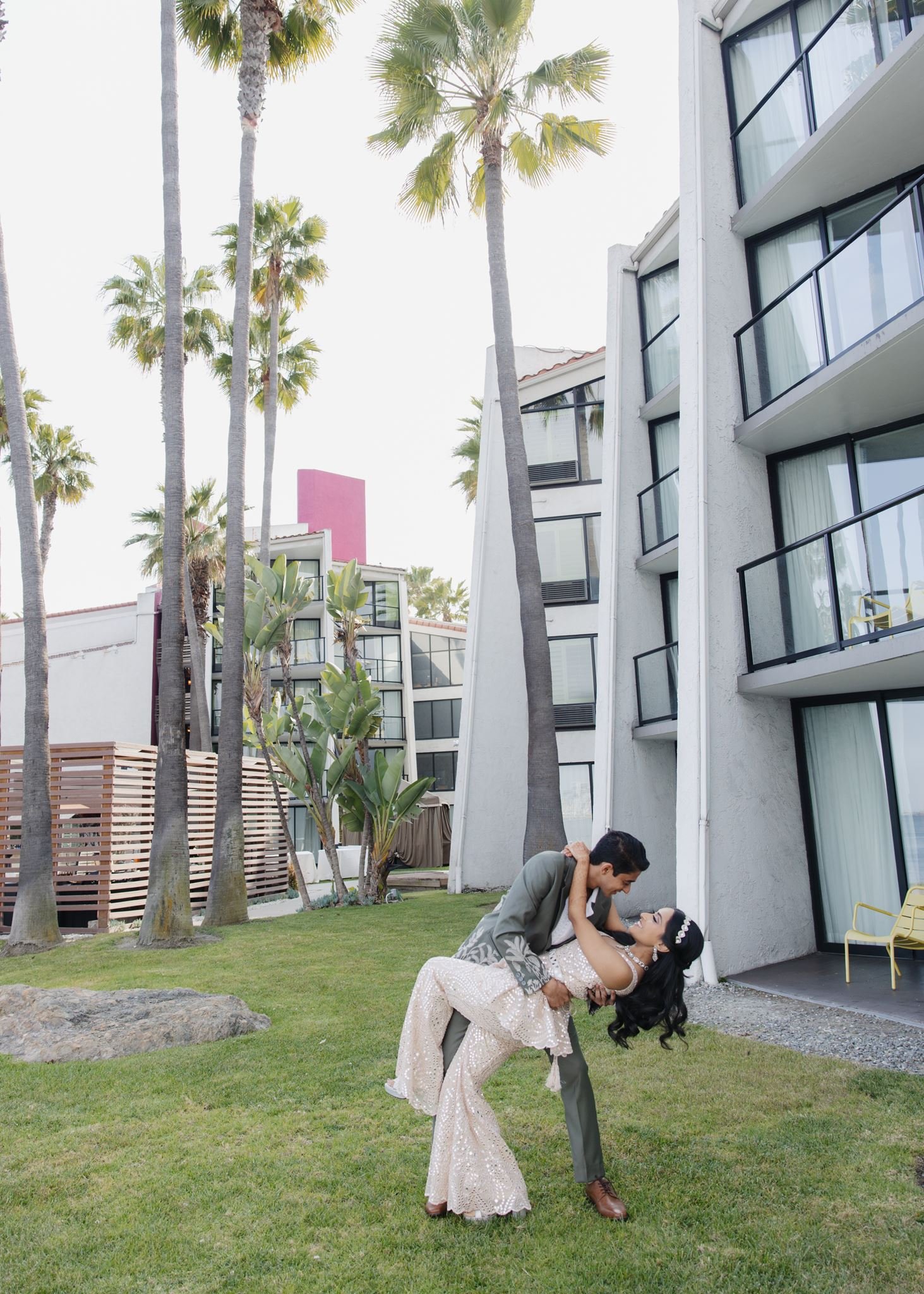 Groom dipping the bride on the lawn beside the hotel's modern wing and palms at Hotel Maya