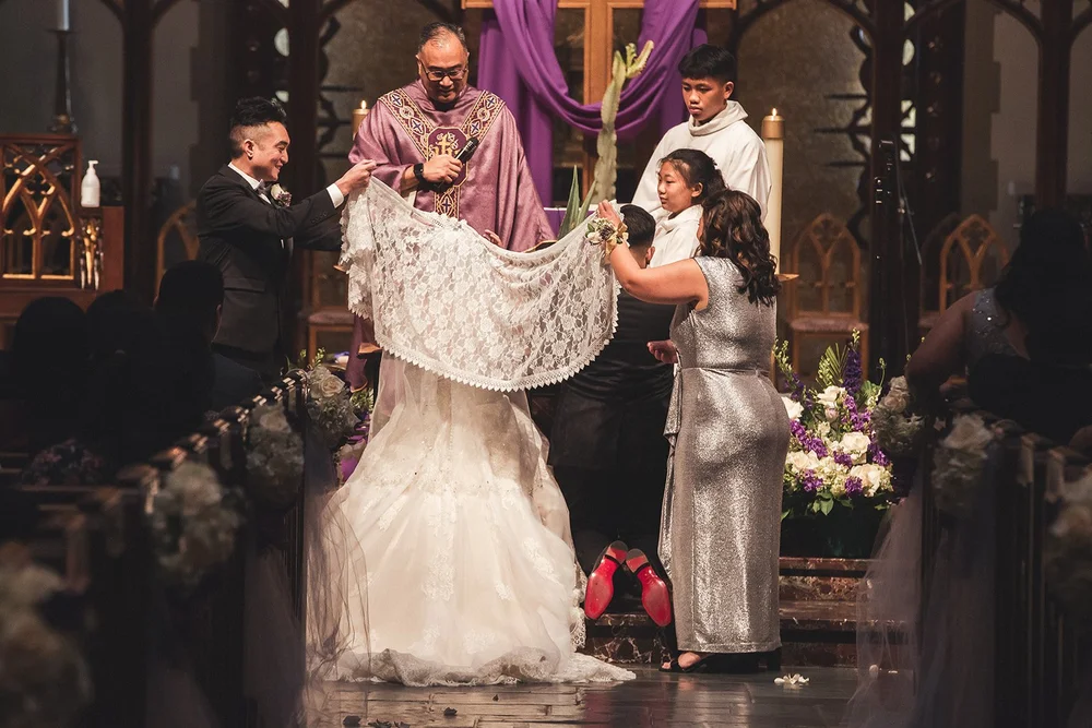 Veil sponsors pinning the veil over the couple during a Filipino Catholic wedding Mass