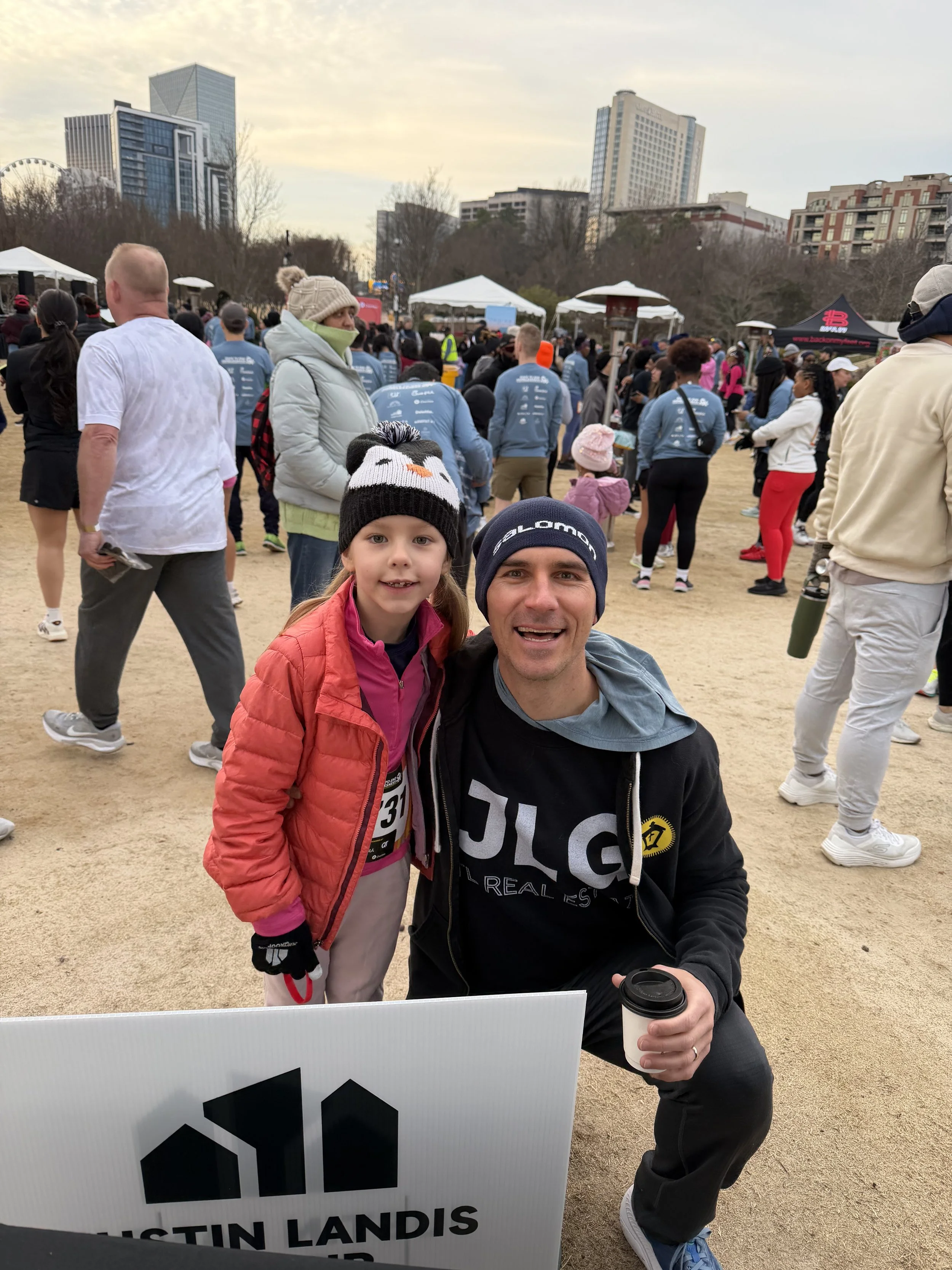 Justin Landis Group team at the Atlanta Mission 5K Race to End Homelessness in downtown Atlanta, holding a JLG sign with the Atlanta skyline in the background