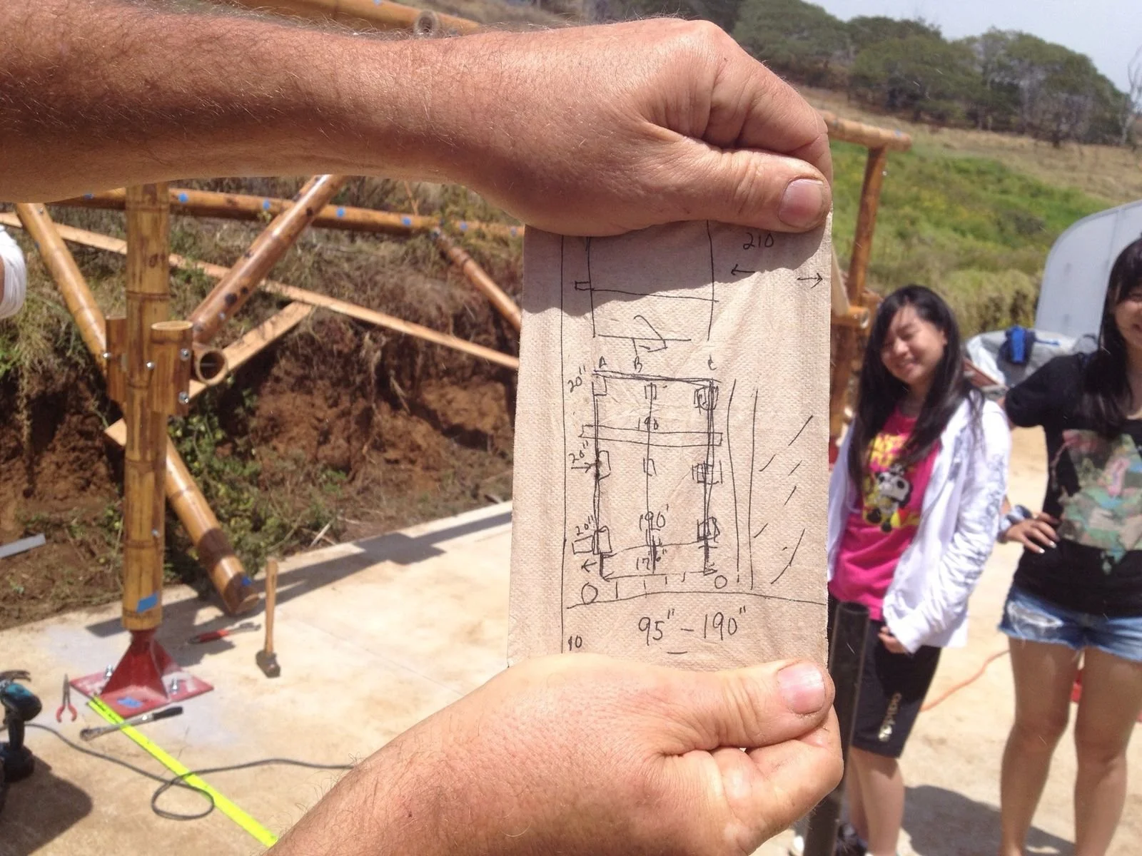 Bobby holding napkin sketch with bamboo structure rising behind