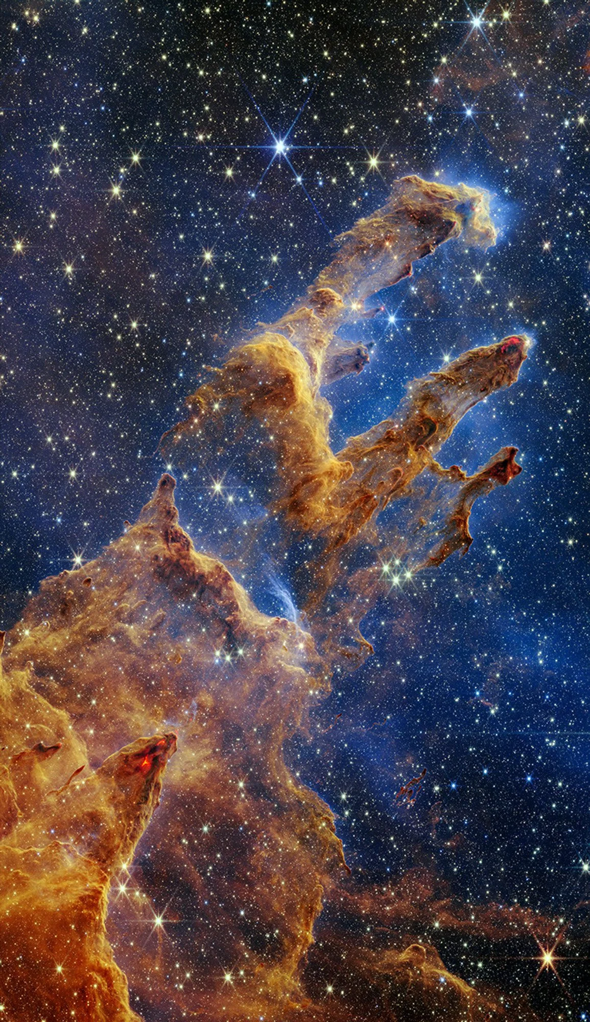 James Webb Space Telescope near-infrared image of the Pillars of Creation, showing semi-transparent towers of gas and dust surrounded by a dense field of stars.