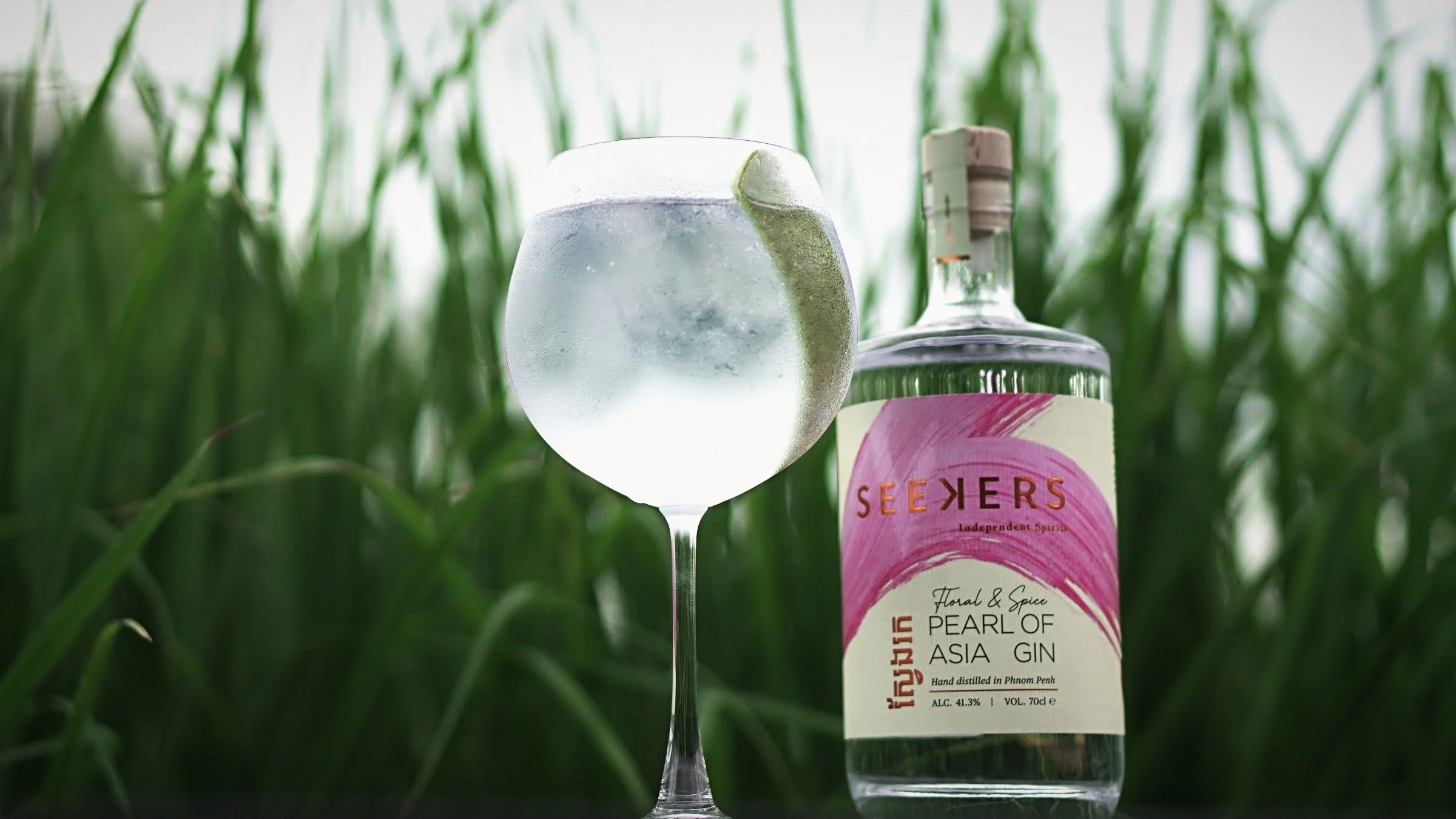 A glass of Pearl of Asia gin and tonic and the bottle standing in the lemongrass at the distillery garden