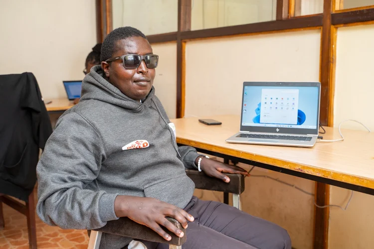 A photo of Elijah Karue sitting, on a desk, with a computer in front of him. 