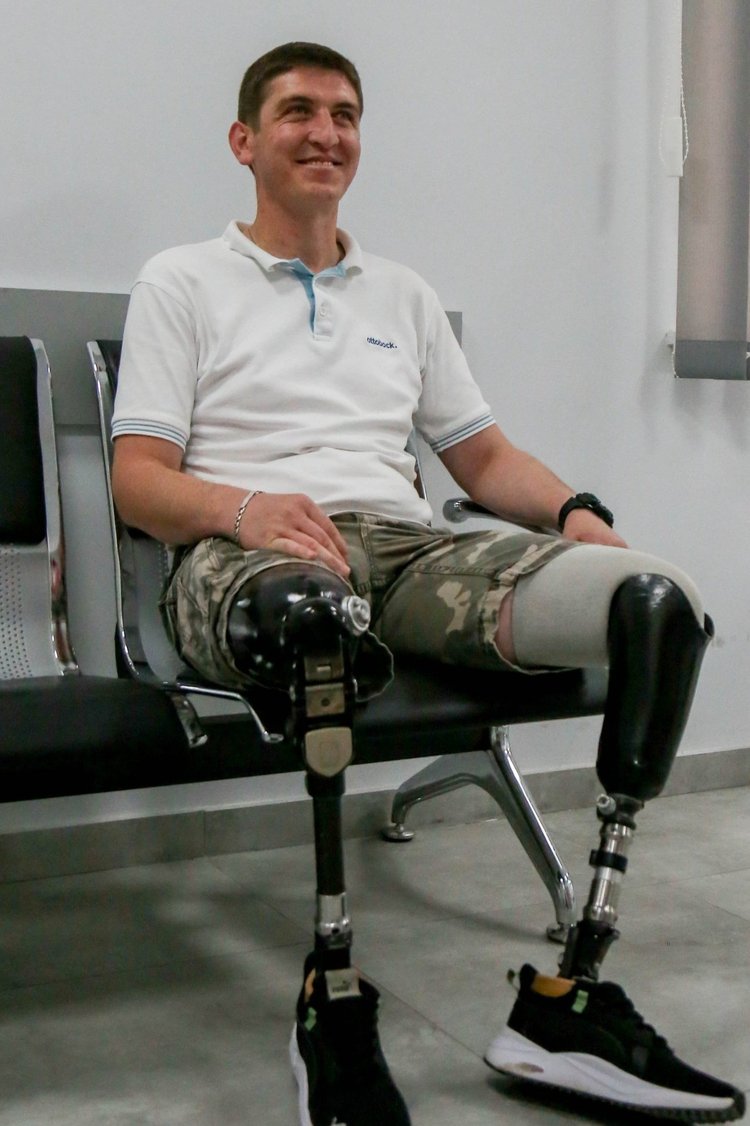 Photograph of Giorgi Shekiladze, 32, from Georgia, a war veteran who served in Iraq. He has two prosthetic legs.  Sitting on a chair smiling 