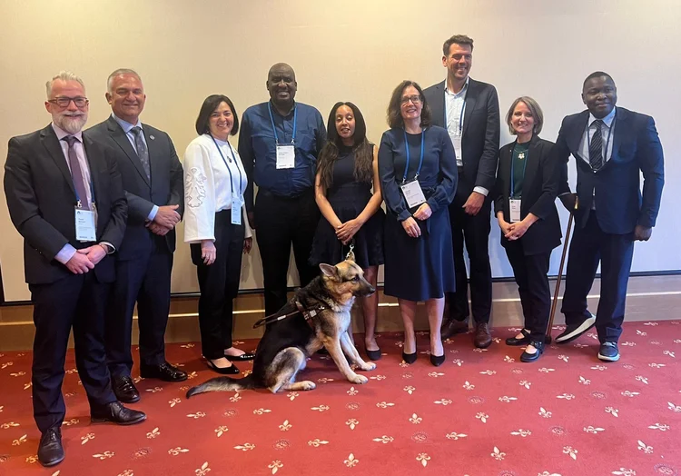 A group photo of nine speakers of the  World health summit speakers standing and dog in the middle 