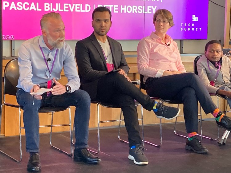 ATscale CEO Pascal Bijleveld speaking at the Remarkable Tech summit with Varun Chandak, Catherine Holloway, and Bernard Chiira.  All are sitting on chairs in a line for the panel discussion