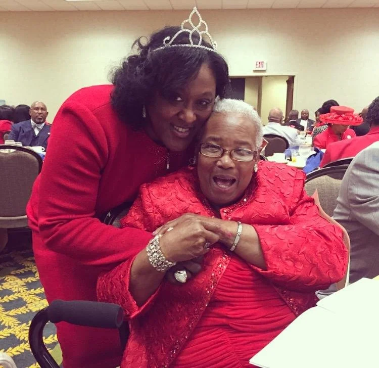 Lady Gail Booker wearing a crown and embracing an older woman at a church gathering
