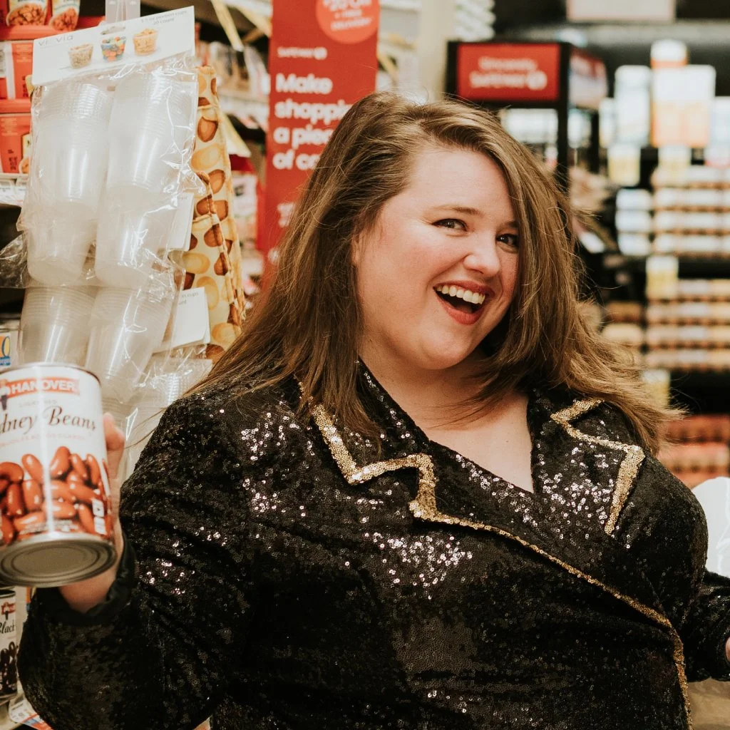 Louisa, wearing a shiny sequin top, shows off a can of beans